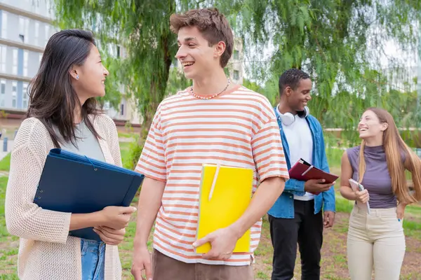 Kampüsteki müfredat notlarını incelerken konuşan ve gülen mutlu üniversite öğrencileri. Çeşitli Asya ve Avrupa gençliği