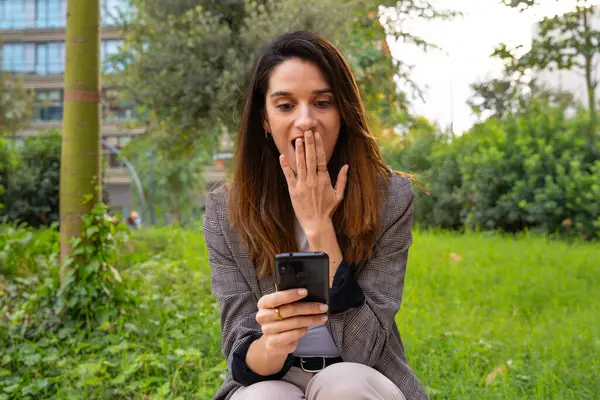 Young woman with cell phone in her hands, writes messages and reads news online, using an app with a surprised gesture.