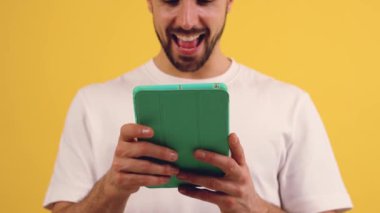 Tablet kullanan mutlu bir adamın portresi sarı monokromatik stüdyo arka planında mesaj atıyor. İnsan duyguları kavramı, yüz ifadesi. İlanınız için boşluk kopyala