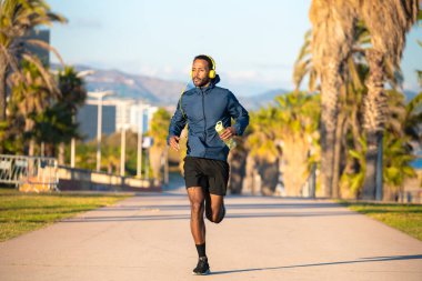  Kulaklık takan genç koşucu elinde soğuk izotonik spor suyu tutuyor..