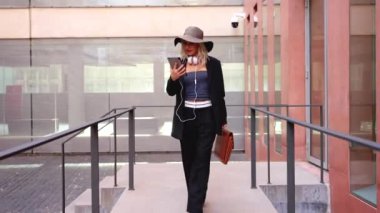 Satisfied with the results, the businesswoman walking down the street outside the office building, a boss holds a phone in her hands, writes messages and reads news online, using an app.