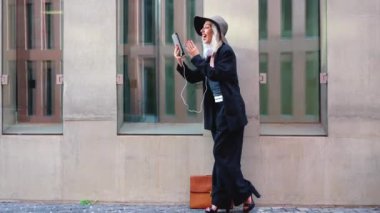  Beyaz iş kadını ofis binasının önünde caddede yürüyor, patron elinde dijital tabletle profesyonel bir meslektaşıyla konuşuyor.