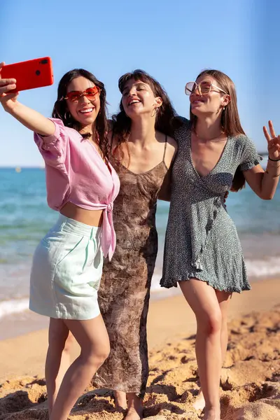 Bir grup gülümseyen, etnik çeşitlilikte kadın tatilde. Neslin güzel ve neşeli kızları cep telefonlu bir fotoğraf için poz verir..