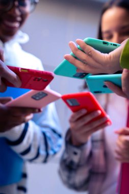 Dikey portre tanımlanamayan arkadaş grubu akıllı telefonlarına bakıyor. Çok ırklı gençler kampüste cep telefonlarıyla internette geziniyorlar.