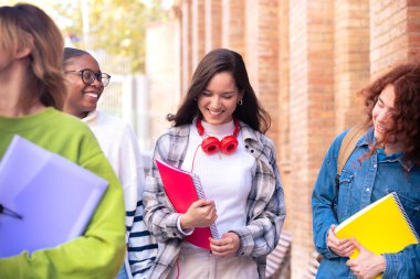 Üniversite kampüsünde dolaşan çok ırklı bir grup öğrenci açık havada gülüyor. Gençler birlikte eğleniyor..