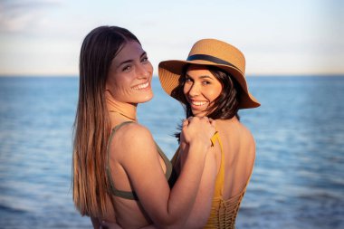 Güneş gözlüklü neşeli çoklu etnik arkadaşlar sahilde mutlu bir şekilde kameraya bakıyorlar..