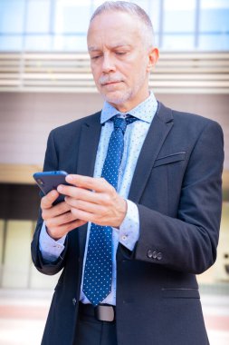 Sonuçlardan memnun olan işadamı ofis binasının dışındaki sokakta yürüyor, olgun bir patron elinde telefon ve kahve tutuyor, bir uygulama kullanarak mesajlar yazıyor ve internetten haberleri okuyor..