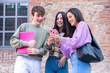 Dışarıda oturan mutlu çok ırklı öğrenciler internette sohbet etmek için cep telefonu kullanıyorlar. Üniversite yaşam konsepti
