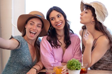 Bir grup gülümseyen, etnik çeşitlilikte kadın tatilde. Neslin güzel ve neşeli kızları cep telefonlu bir fotoğraf için poz verir..