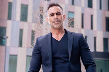 Beyaz bir iş adamının dış mekanda duran takım elbiseli kameraya yakından baktığı bir fotoğraf. Düşünceli bir ifadeyle genç bir avukatın bakışları.