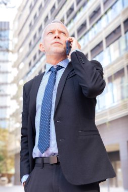 Sonuçlardan memnun olan işadamı, ofis binasının önündeki caddede yürüyor. Olgun bir patron telefonla konuşuyor.