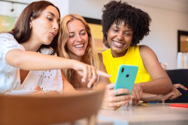 Üç genç arkadaş telefonda sosyal medyaya bakarken bir şeyi işaret ediyor..