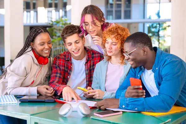 Beş mutlu öğrenciden oluşan bir grup üniversitede açık havada akıllı telefon kullanıyor. Modern, teknoloji dostu bir ortamda meşgul, işbirliği ve öğrenme deneyimlerinin tadını çıkarıyorlar.