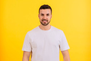 Gülümseyen genç bir adam parlak sarı bir arka planın önünde duruyor, düz beyaz bir tişört giyiyor. Dost canlısı ve kendinden emin bir ifadesi var. Sıradan ve cana yakın bir görünüm sergiliyor..
