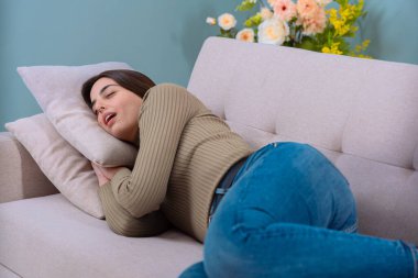 A young woman is lying on a sofa, resting her head on a pillow, and relaxing at home. The scene shows comfort, calm, and leisure, with a cozy atmosphere. clipart