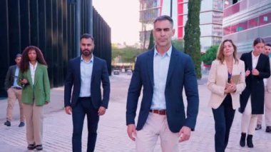 Çeşitli profesyonellerden oluşan bir iş ekibi modern bir şehir caddesinde güvenle yürüyor. İş kıyafetleri giyiyorlar ve şirket ortamında birlikte çalışıyorlar..