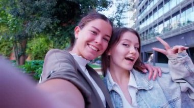 İki kadın şehir dışında alışveriş yaparken akıllı telefonuyla mutlu bir şekilde selfie çekiyor. Gülümsüyorlar ve ellerinde alışveriş torbalarıyla birlikte vakit geçiriyorlar.