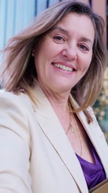 Neşeli genç bir kadının portresi, yüksek binalar ve canlı mimariyle modern şehir ortamında güvenle gülümsüyor..