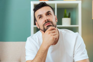 Beyaz adam evdeki kanepede oturuyor. Vücudunu ileri çekiyor. İçerideki kameraya dikkatlice bakıyor.