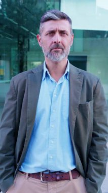 Neşeli genç bir adamın portresi, yüksek binalar ve canlı mimari ile modern bir şehir ortamında güvenle gülümsüyor..