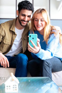 Neşeli bir çift rahat bir kanepede oturur ve görüntülü konuşma sırasında gülümser ve akıllı telefona el sallarlar. Onların mutlu ifadeleri ve rahat ayarlı bağlantı, teknoloji ve ilişkileri. Dikey