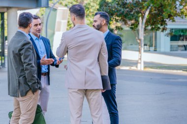 Group of four businessmen in formal and smart casual attire discussing outdoors in a modern urban setting, demonstrating teamwork and collaboration.  clipart