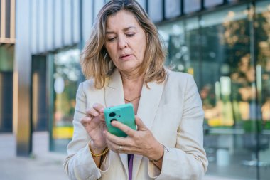Modern bir şehir ortamında akıllı telefon kullanarak gülümseyen orta yaşlı iş kadını..