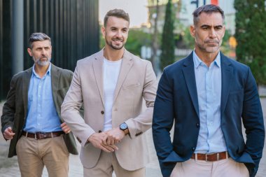  Açık havada resmi ve yarı resmi giyinmiş üç iş adamından oluşan bir grup. Modern kentsel ortam profesyonelliği, liderliği ve işbirliğini vurguluyor