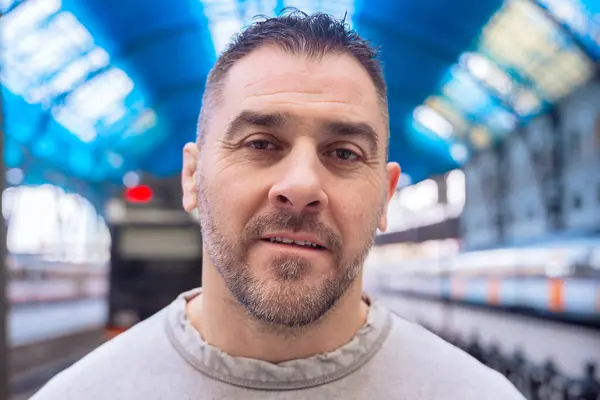  Gri kazaklı, orta yaşlı bir adamın tren istasyonuna dik dik bakışları. Düşünceli ifadesi, şehir ortamında odaklanmayı, beklemeyi ve derin düşüncelere sahip olduğunu gösteriyor..