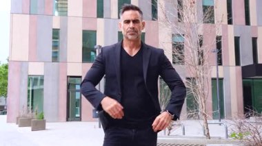  Siyah takım elbiseli profesyonel bir işadamı modern bir şehirde kollarını kavuşturmuş duruyor. Güçlü duruşu ve ciddi ifadesi güven, otorite ve liderlik taşıyor.. 