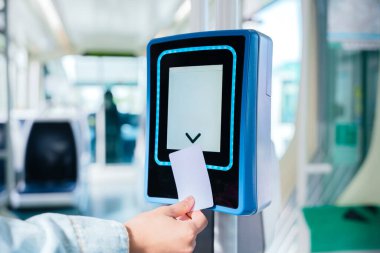 Toplu taşıma içine elektronik tasdik makinesine bilet sokan bir elin yakın çekimi. Modern dijital sistem, yolcuların seyahat erişimlerini verimli bir şekilde doğrulamalarına olanak sağlıyor..