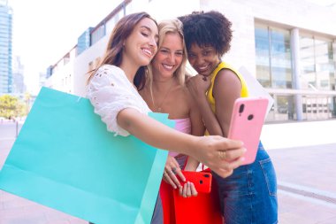 Üç genç kadın dışarıda oturuyor, gülümsüyor ve birlikte eğlenceli bir selfie çekiyorlar. Arkadaşlık, mutluluk, sosyal medya ve açık hava yaşam tarzı gibi kavramlar için mükemmel..