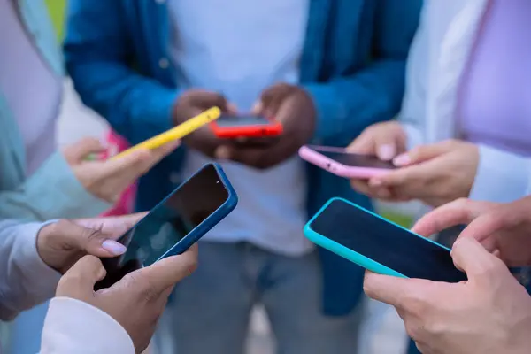 Tanımlanamayan arkadaş grubu akıllı telefonlarına bakıyor. Çok ırklı gençler kampüste cep telefonlarıyla internette geziniyorlar.