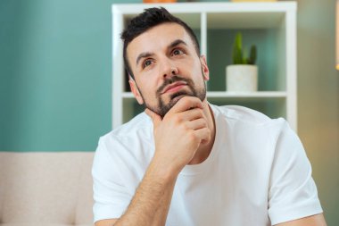 Beyaz adam evdeki kanepede oturuyor. Vücudunu ileri çekiyor. İçerideki kameraya dikkatlice bakıyor.