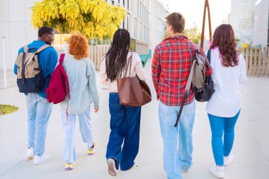 Bir grup öğrenci dışarıda birlikte yürürken gülümsüyor. Ellerinde defterler ve klasörler tutuyorlar, gündelik kıyafetler giyiyorlar ve parlak, modern bir ortamda vakit geçiriyorlar..