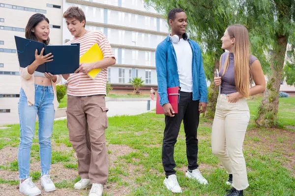 Kampüsteki müfredat notlarını incelerken konuşan ve gülen mutlu üniversite öğrencileri. Çeşitli Asya ve Avrupa gençliği