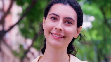 Kapalı gözleri ve koyu renk saçları olan açık hava ortamında duran genç bir kadının yakın plan portresi. Bulanık yeşil arka plan görüntüye sakinleştirici, doğal bir atmosfer ekler..