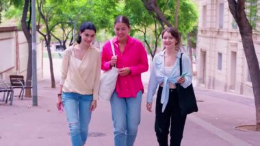 Üç gülümseyen genç kadın ağaçlarla kaplı bir cadde boyunca yürüyorlar, sohbet ediyorlar. Günlük giysiler içinde, şehir ortamında mutlu ve rahat bir anı paylaşıyorlar..
