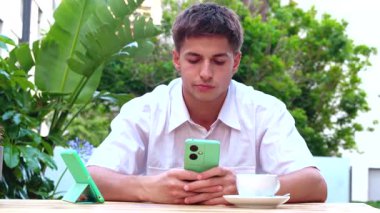 Ciddi yakışıklı, genç, konsantre olmuş üzgün adam cep telefonuna bakıyor açık kafedeki terasta mesaj yazıyor. Sosyal medya bağımlılığı. uygulamalar, aygıtlar teknoloji kavramı