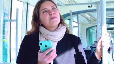 Trenle seyahat ederken ayakta duran akıllı telefonu kullanan beyaz bir kadın. Toplu taşıma araçlarını kullanan güzel, genç bir kadın..