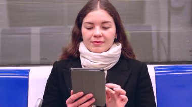 Trenle seyahat ederken tablet kullanan beyaz bir kadın. Genç ve güzel bir kadın toplu taşıma araçlarını kullanıyor. Şehir ışığı tarafından aydınlatıldı. Dikey