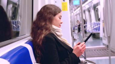 Trenle seyahat ederken tablet kullanan çekici beyaz bir kadın. Genç ve güzel bir kadın toplu taşıma araçlarını kullanıyor. Şehir ışığı tarafından aydınlatıldı. Dikey