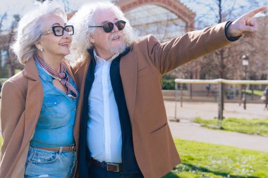 Gri saçlı, mutlu, beyaz bir çift şehri keşfederken güneşli bir günün tadını çıkarıyor. Zarif yaşlı adam şık kadın gülümserken ileri bakar.. 