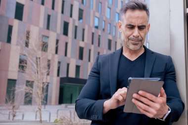 Modern bir ofis binasının dışında tablet üzerinde çalışan kendinden emin bir iş adamı. Kopya alanı olan şehir ayarı. İş, teknoloji, üretkenlik ve profesyonel yaşam tarzı temaları için ideal.