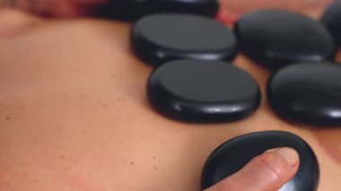 Sıcak taş masajının yakın görüntüsü, rahatlatıcı bir terapi seansı sırasında sırtüstü uzanmış siyah taşlar. Spa, sağlık, şifa ve alternatif sağlık kavramları için mükemmel.. 