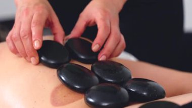 Sıcak taş masajının yakın görüntüsü, rahatlatıcı bir terapi seansı sırasında sırtüstü uzanmış siyah taşlar. Spa, sağlık, şifa ve alternatif sağlık kavramları için mükemmel.. 