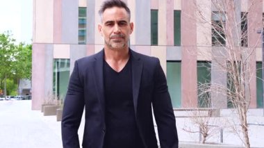 Yatay portre işadamı kollarını kavuşturup doğrudan kameraya bakıyor. Kendine güveni tam ifadesi, siyah kıyafeti ve iş alanı geçmişi liderlik ve profesyonelliği yansıtıyor..