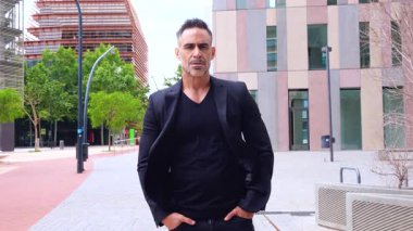 Kafkas işadamı elleri cepte, modern bir iş bölgesinde kameraya bakıyor. Ciddi ifadesi ve kendine güveni başarıyı, liderliği ve kararlılığı yansıtıyor..