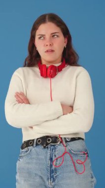 Kolları çapraz beyaz bir kadının dikey portresi ve iğrenç bir yüz ifadesi. Boynuna kulaklık takıyor ve sıradan tarzda mavi bir arka plana karşı duruyor.. 