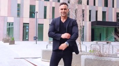 Yatay portre işadamı kollarını kavuşturup doğrudan kameraya bakıyor. Kendine güveni tam ifadesi, siyah kıyafeti ve iş alanı geçmişi liderlik ve profesyonelliği yansıtıyor..